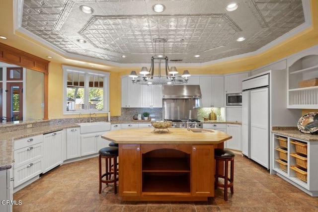 kitchen with white cabinetry, a center island with sink, a kitchen breakfast bar, built in appliances, and pendant lighting