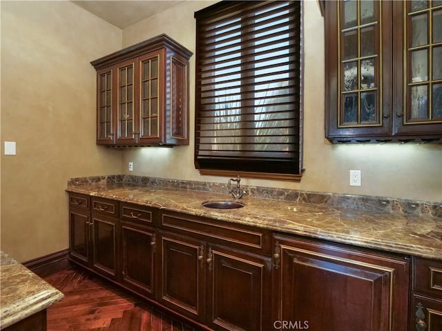 kitchen with dark brown cabinetry, glass insert cabinets, dark wood finished floors, and a sink