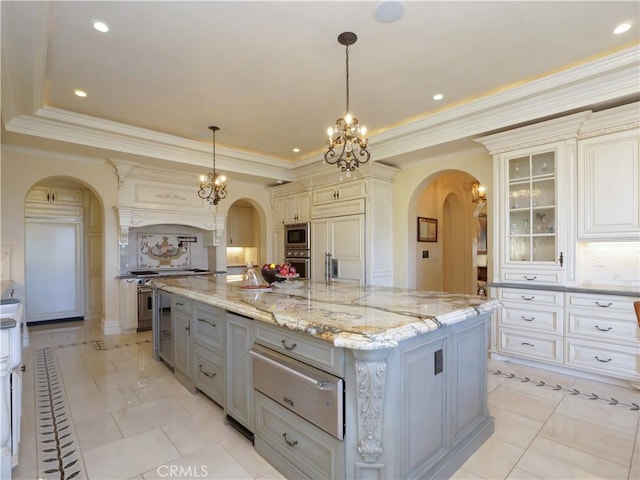 kitchen with arched walkways, a warming drawer, a spacious island, an inviting chandelier, and built in appliances