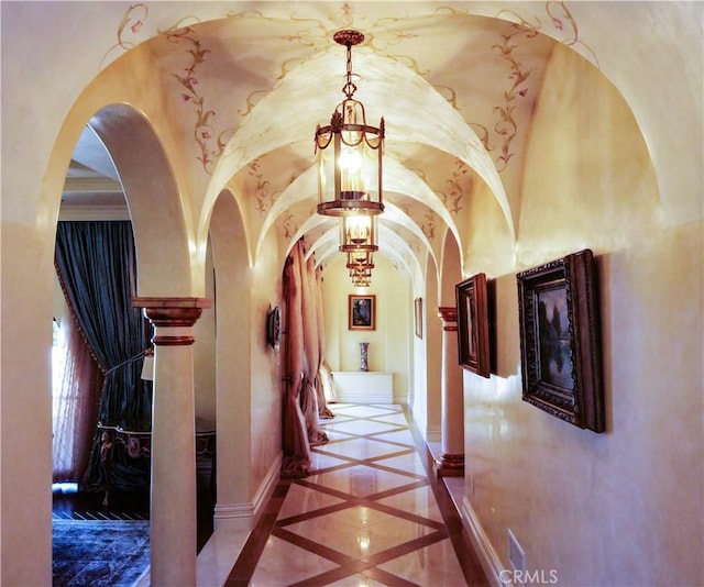 hallway featuring an inviting chandelier, vaulted ceiling, baseboards, and arched walkways