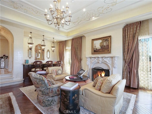 sitting room featuring arched walkways, a premium fireplace, ornamental molding, a raised ceiling, and an inviting chandelier