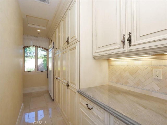 kitchen featuring light tile patterned floors, baseboards, cream cabinetry, and backsplash