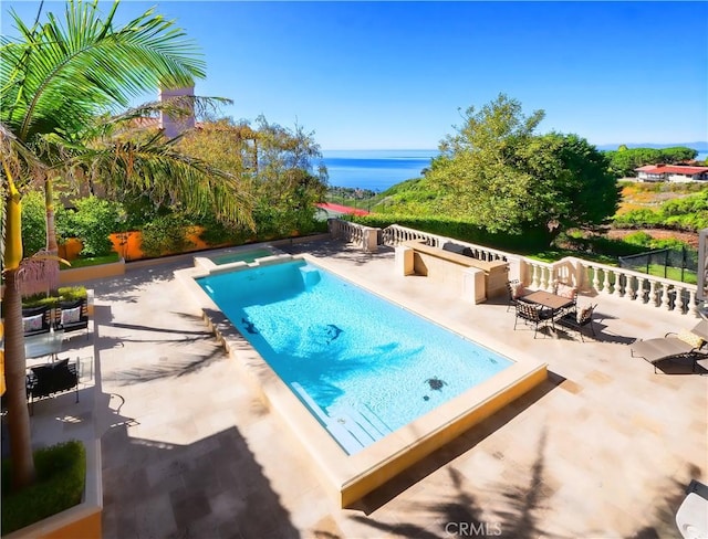 view of swimming pool featuring a water view, a patio area, a pool with connected hot tub, and fence