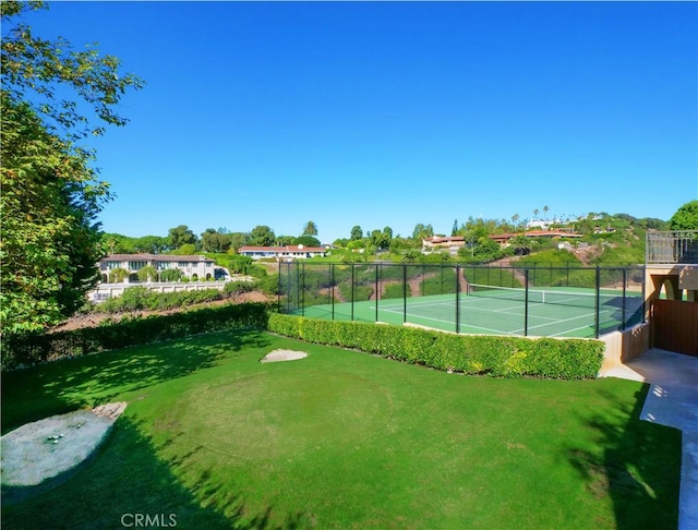 view of tennis court with a yard and fence