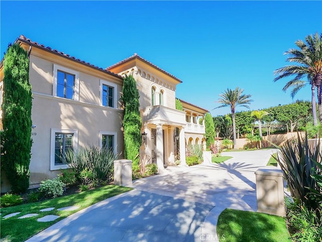 mediterranean / spanish-style house with a balcony, a tile roof, concrete driveway, and stucco siding