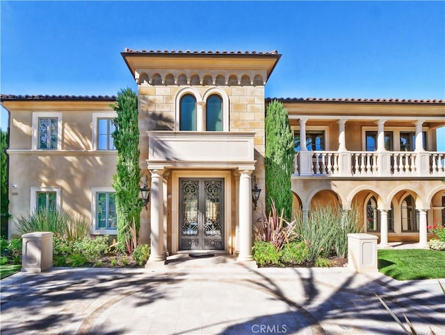 view of front of property featuring french doors, a tile roof, stucco siding, a balcony, and stone siding