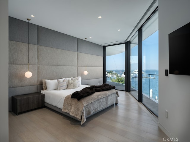 bedroom featuring floor to ceiling windows, a water view, access to outside, and light hardwood / wood-style floors