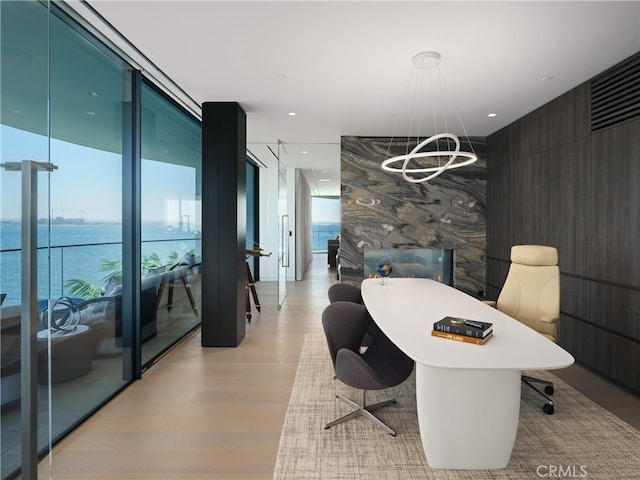 home office with a notable chandelier, a water view, floor to ceiling windows, and light hardwood / wood-style flooring