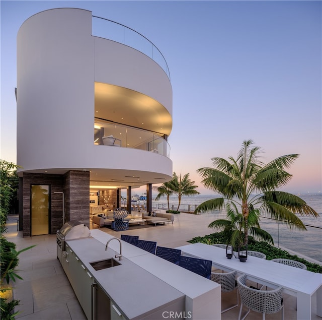 patio terrace at dusk with a water view, sink, an outdoor kitchen, and an outdoor living space