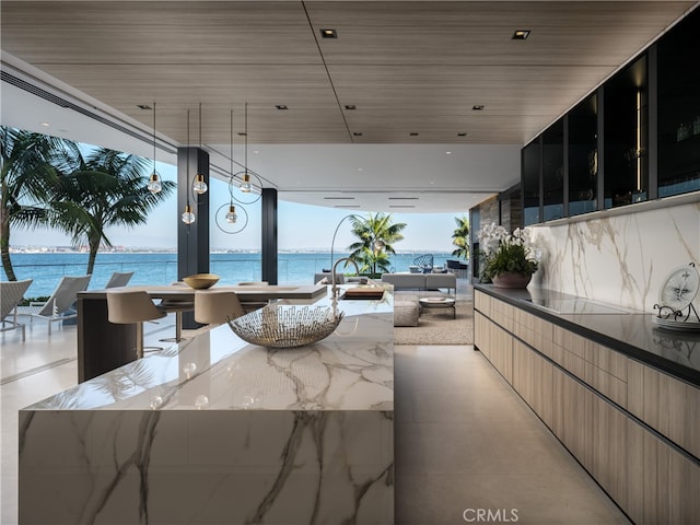 kitchen with black electric cooktop, a water view, dark stone countertops, and a kitchen island with sink