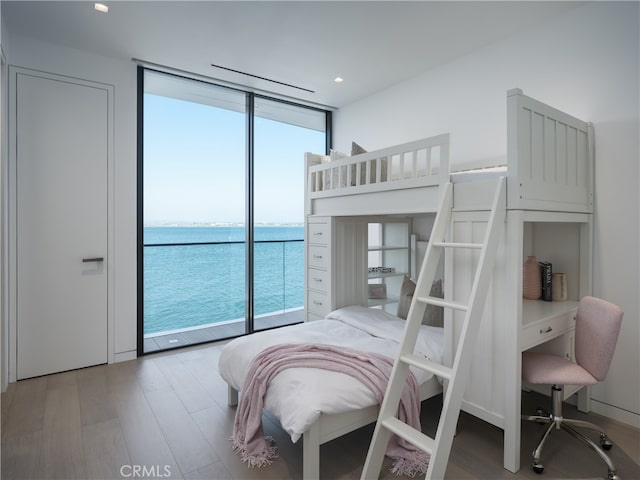 bedroom featuring access to outside, multiple windows, wood-type flooring, and a water view