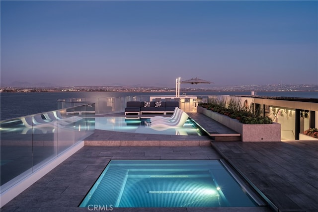 pool at dusk featuring a patio, a water view, outdoor lounge area, and an in ground hot tub