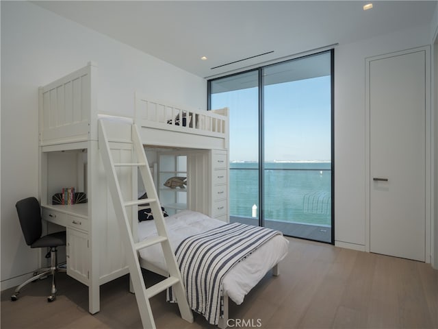 bedroom with a water view, light wood-type flooring, access to outside, and a wall of windows