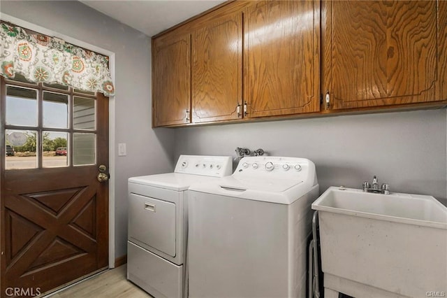 washroom featuring washing machine and clothes dryer, light hardwood / wood-style floors, cabinets, and sink