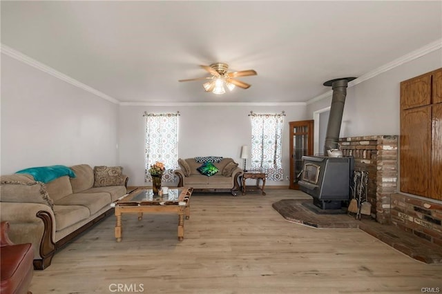 living room with light hardwood / wood-style flooring, a wood stove, ceiling fan, and ornamental molding