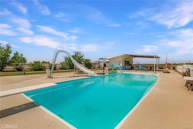 view of pool with a diving board, a water slide, and a patio