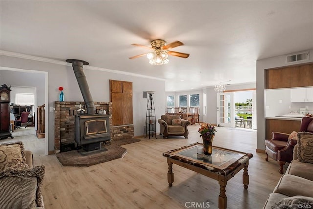 living room featuring a wood stove, light hardwood / wood-style floors, ceiling fan with notable chandelier, and ornamental molding