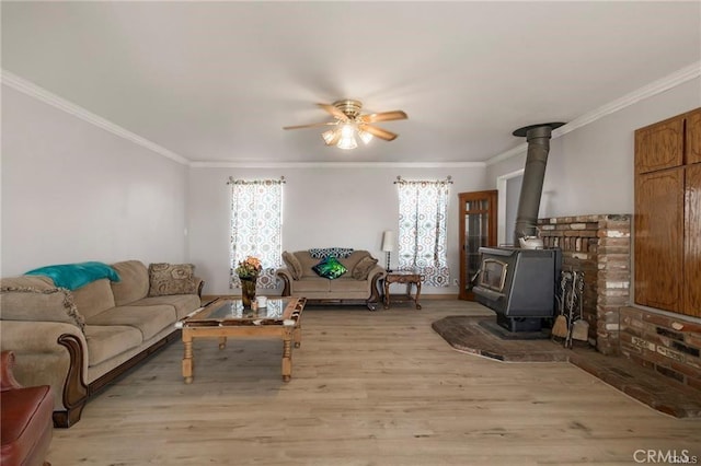 living room featuring a wood stove, ceiling fan, light hardwood / wood-style flooring, and ornamental molding