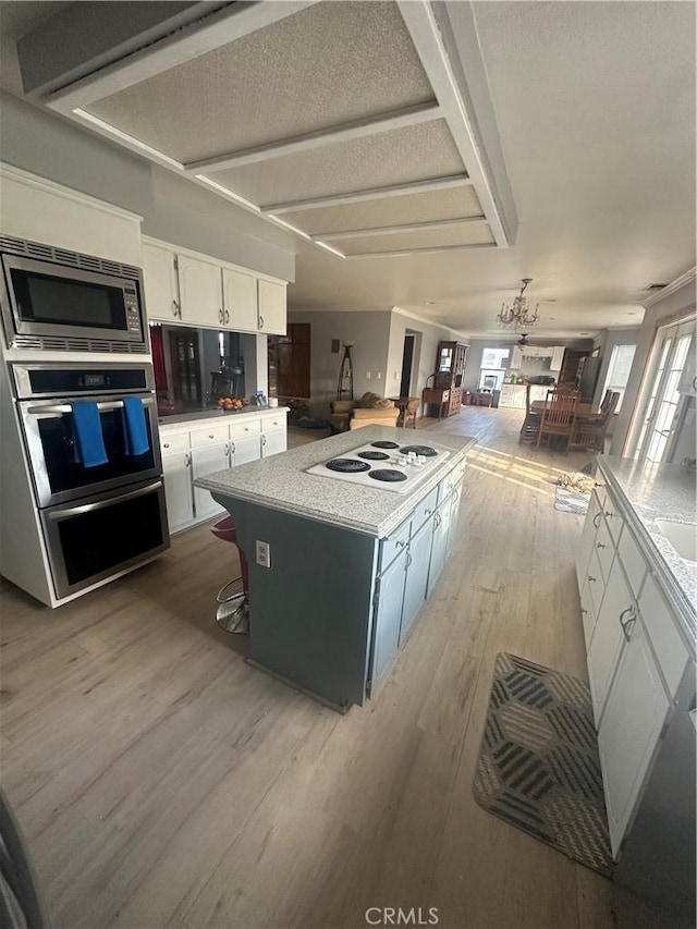 kitchen with appliances with stainless steel finishes, a textured ceiling, light hardwood / wood-style flooring, a center island, and white cabinetry