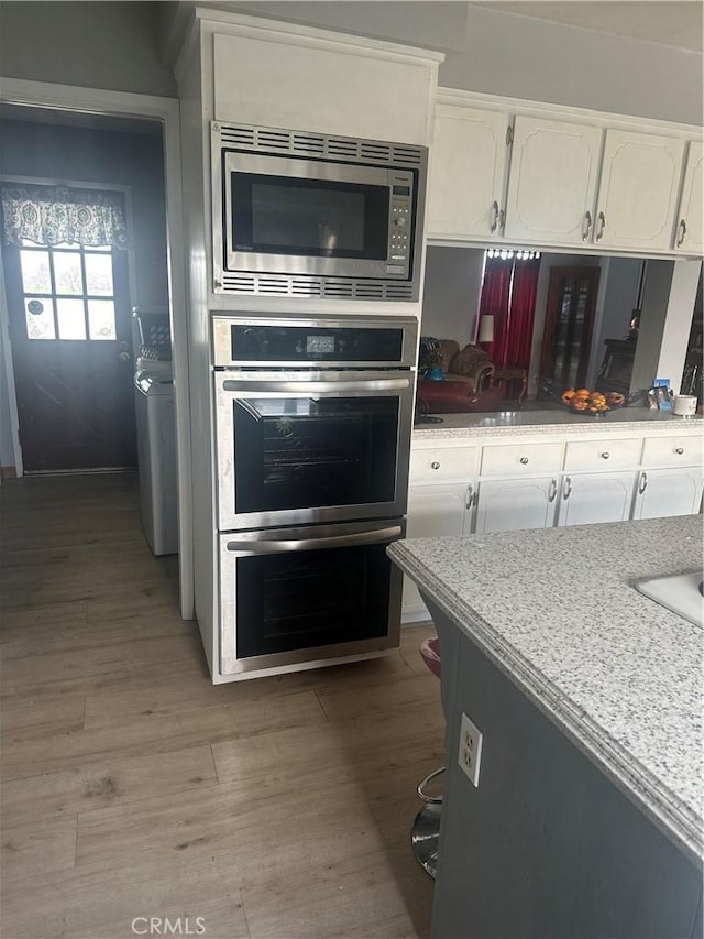 kitchen featuring washer / clothes dryer, white cabinets, stainless steel appliances, and light wood-type flooring