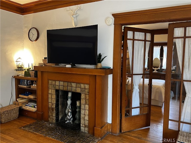 living room featuring french doors, dark wood-type flooring, a tile fireplace, and crown molding