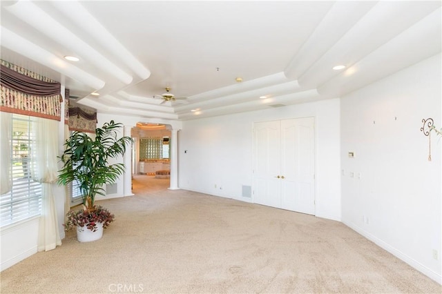 unfurnished room featuring a raised ceiling, light colored carpet, and ceiling fan