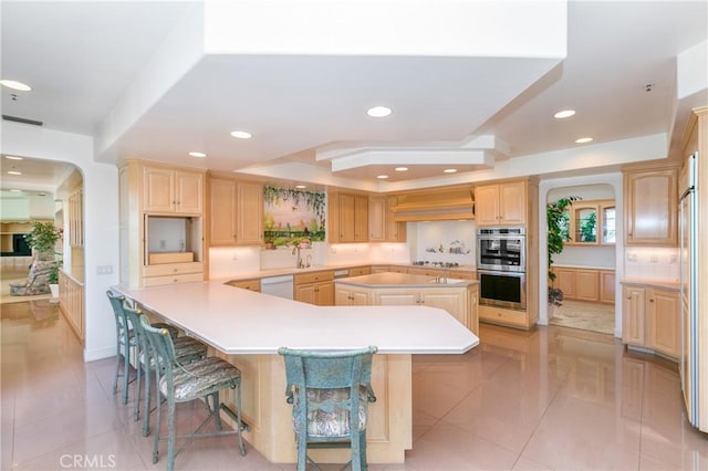 kitchen with stainless steel double oven, a center island, a kitchen bar, light brown cabinets, and light tile patterned floors