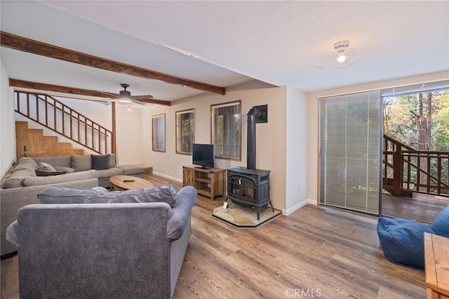 living room featuring ceiling fan, beam ceiling, wood-type flooring, a textured ceiling, and a wood stove