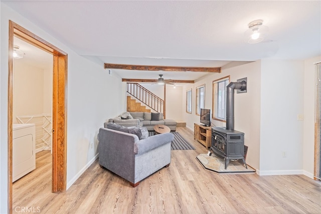 living room featuring beam ceiling, washer / dryer, light wood-type flooring, and a wood stove