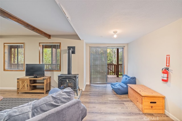 living room featuring beamed ceiling, a wood stove, a textured ceiling, and light wood-type flooring