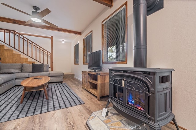 living room featuring ceiling fan, light hardwood / wood-style floors, beamed ceiling, and a wood stove