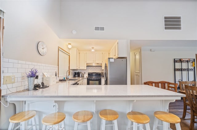 kitchen with sink, stainless steel fridge, a breakfast bar, black / electric stove, and kitchen peninsula