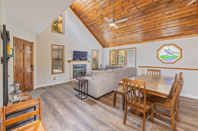 dining area featuring a tiled fireplace, wood-type flooring, wood ceiling, and high vaulted ceiling