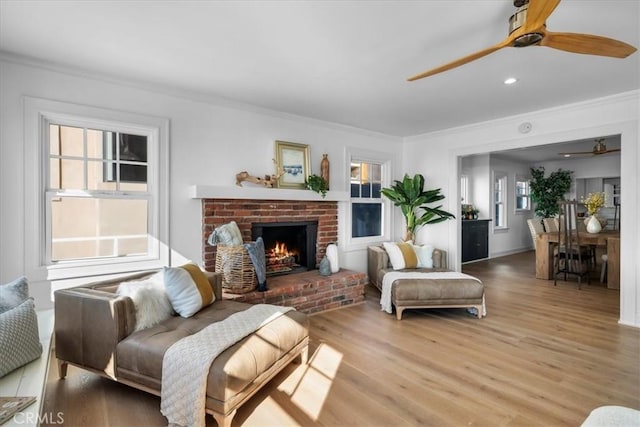 living room featuring a brick fireplace, ornamental molding, and light wood-type flooring