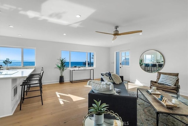 living room featuring ceiling fan, light hardwood / wood-style flooring, a water view, and plenty of natural light