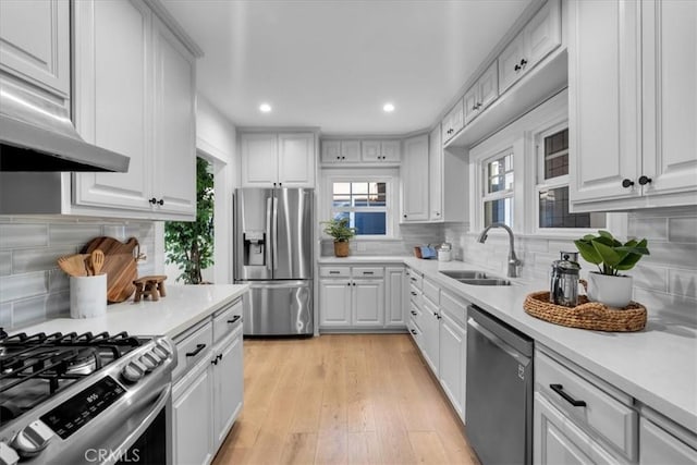 kitchen with sink, light hardwood / wood-style flooring, appliances with stainless steel finishes, tasteful backsplash, and white cabinetry