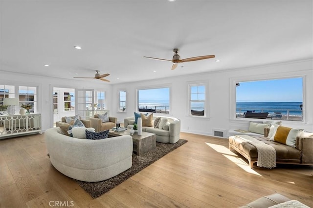 living room featuring a water view, light hardwood / wood-style flooring, plenty of natural light, and ornamental molding