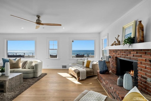 living room featuring ceiling fan, crown molding, light hardwood / wood-style floors, a fireplace, and a water view