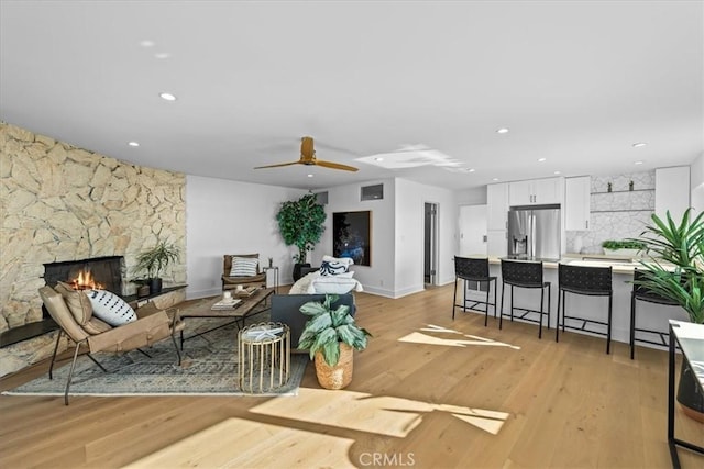 living room with light hardwood / wood-style flooring, ceiling fan, and a stone fireplace