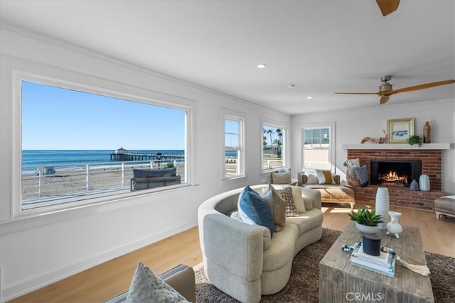 living room featuring ornamental molding, ceiling fan, a water view, hardwood / wood-style flooring, and a fireplace