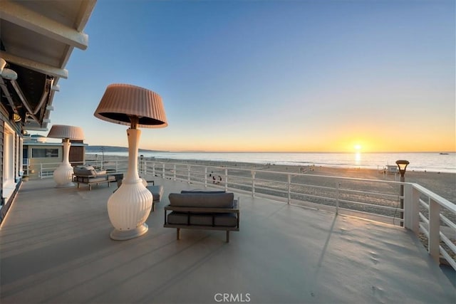 patio terrace at dusk with a balcony, a water view, and a beach view