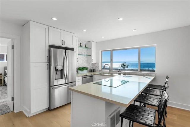 kitchen with white cabinets, a kitchen breakfast bar, a water view, sink, and stainless steel appliances