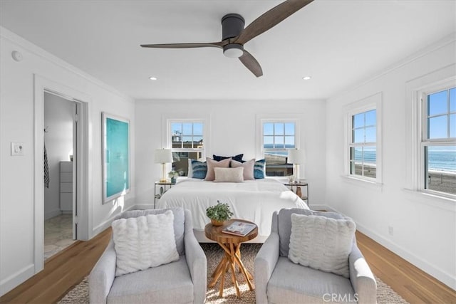 bedroom featuring ceiling fan, light hardwood / wood-style floors, a water view, and crown molding