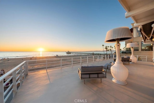 patio terrace at dusk featuring a water view and a view of the beach