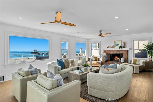 living room featuring a fireplace, a water view, a healthy amount of sunlight, and light wood-type flooring