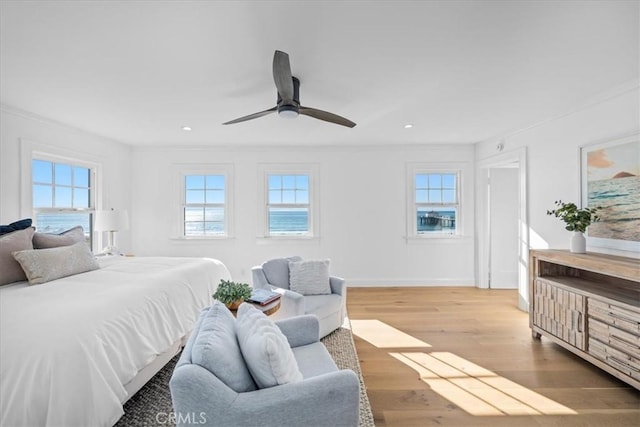 bedroom with hardwood / wood-style flooring, ceiling fan, crown molding, and a water view