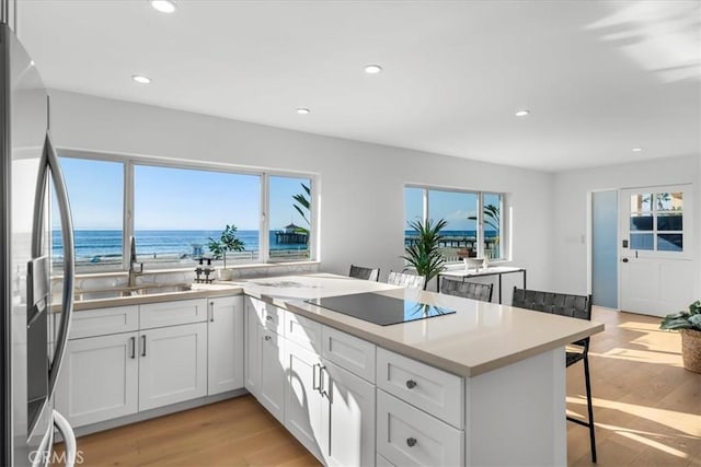 kitchen featuring a breakfast bar, black electric cooktop, a water view, stainless steel fridge with ice dispenser, and white cabinetry