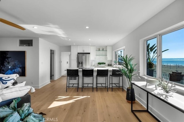 kitchen with white cabinetry, light hardwood / wood-style flooring, stainless steel refrigerator with ice dispenser, a breakfast bar, and a water view