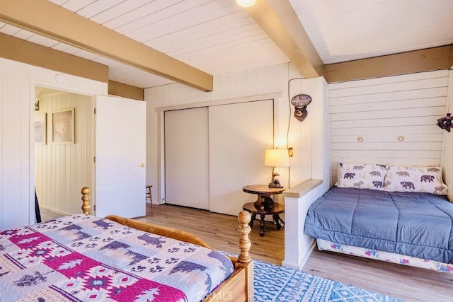 bedroom featuring beamed ceiling, wood-type flooring, wooden walls, and a closet