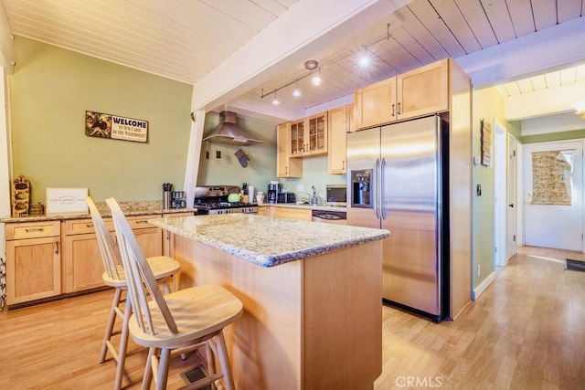 kitchen with a kitchen bar, kitchen peninsula, stainless steel appliances, light stone countertops, and wall chimney range hood